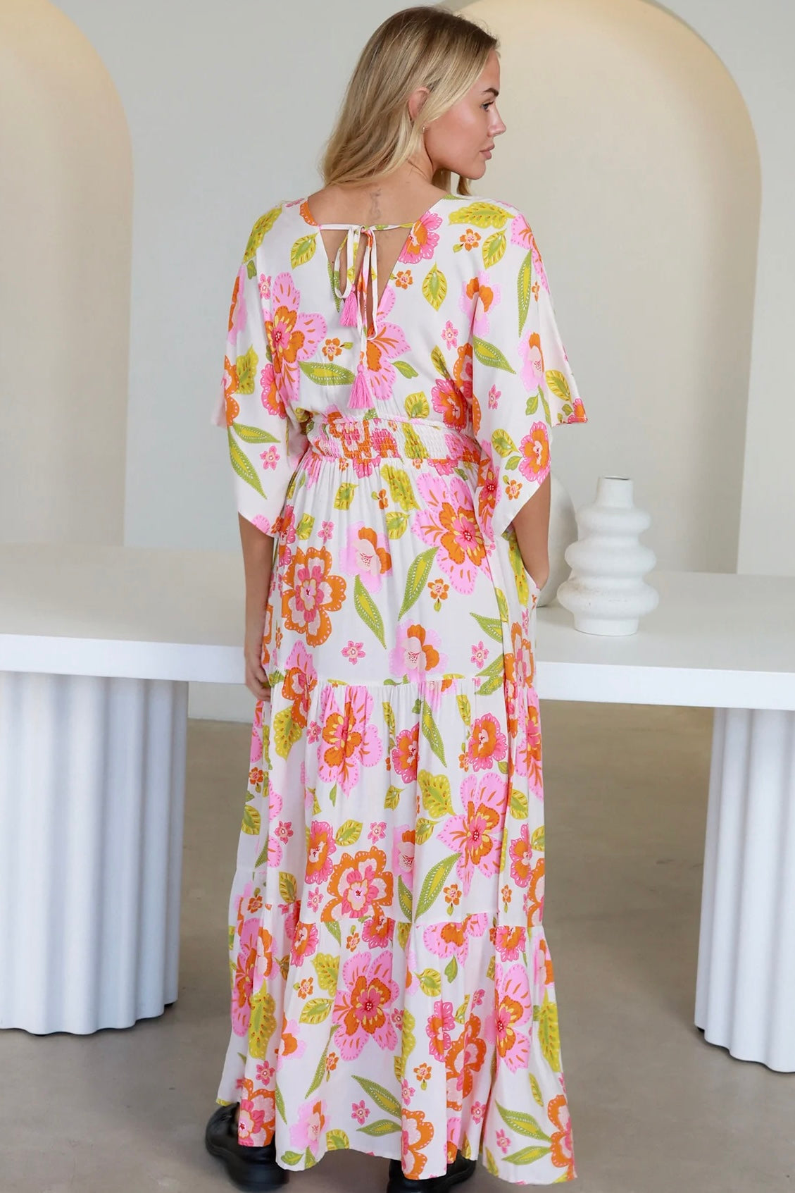 Woman in a coral-pink floral boho maxi dress with kimono sleeves - Isla Grace Tiered Maxi Dress Australia.