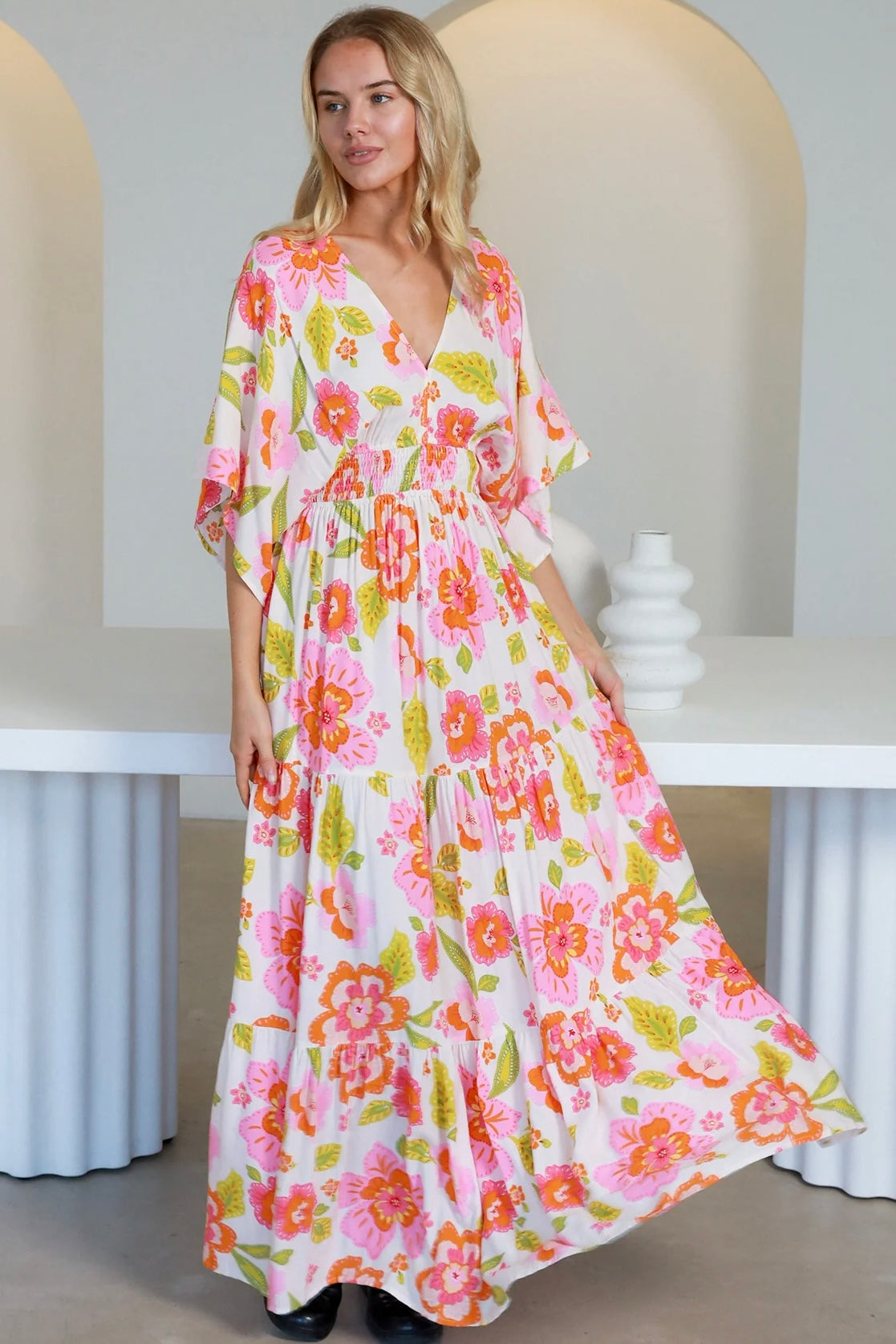 Woman in a coral-pink floral boho maxi dress with kimono sleeves - Isla Grace Tiered Maxi Dress Australia.