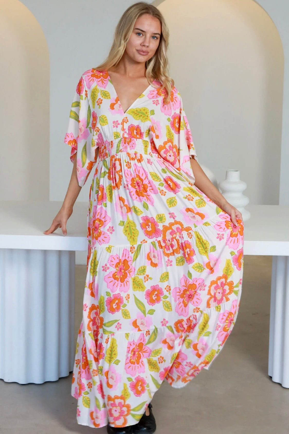 Woman in a coral-pink floral boho maxi dress with kimono sleeves - Isla Grace Tiered Maxi Dress Australia.