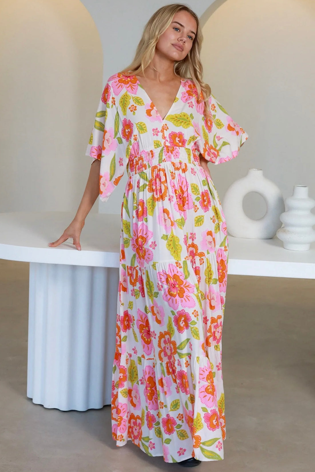 Woman in a coral-pink floral boho maxi dress with kimono sleeves - Isla Grace Tiered Maxi Dress Australia.