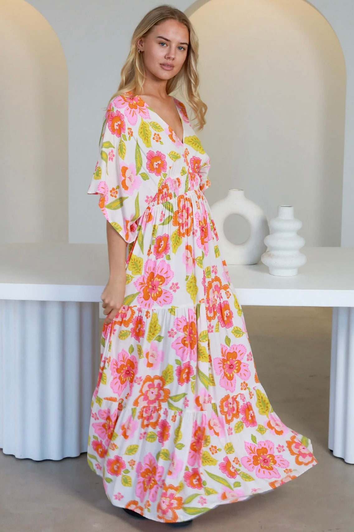 Woman in a coral-pink floral boho maxi dress with kimono sleeves - Isla Grace Tiered Maxi Dress Australia.