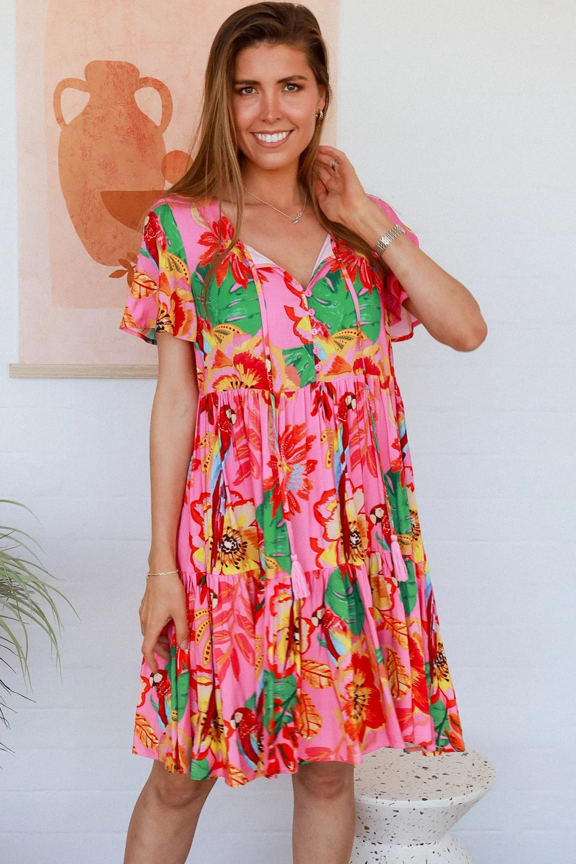 Pink floral mini dress with poppy and parrot print, V-neck button bodice, tassel ties and flutter sleeves