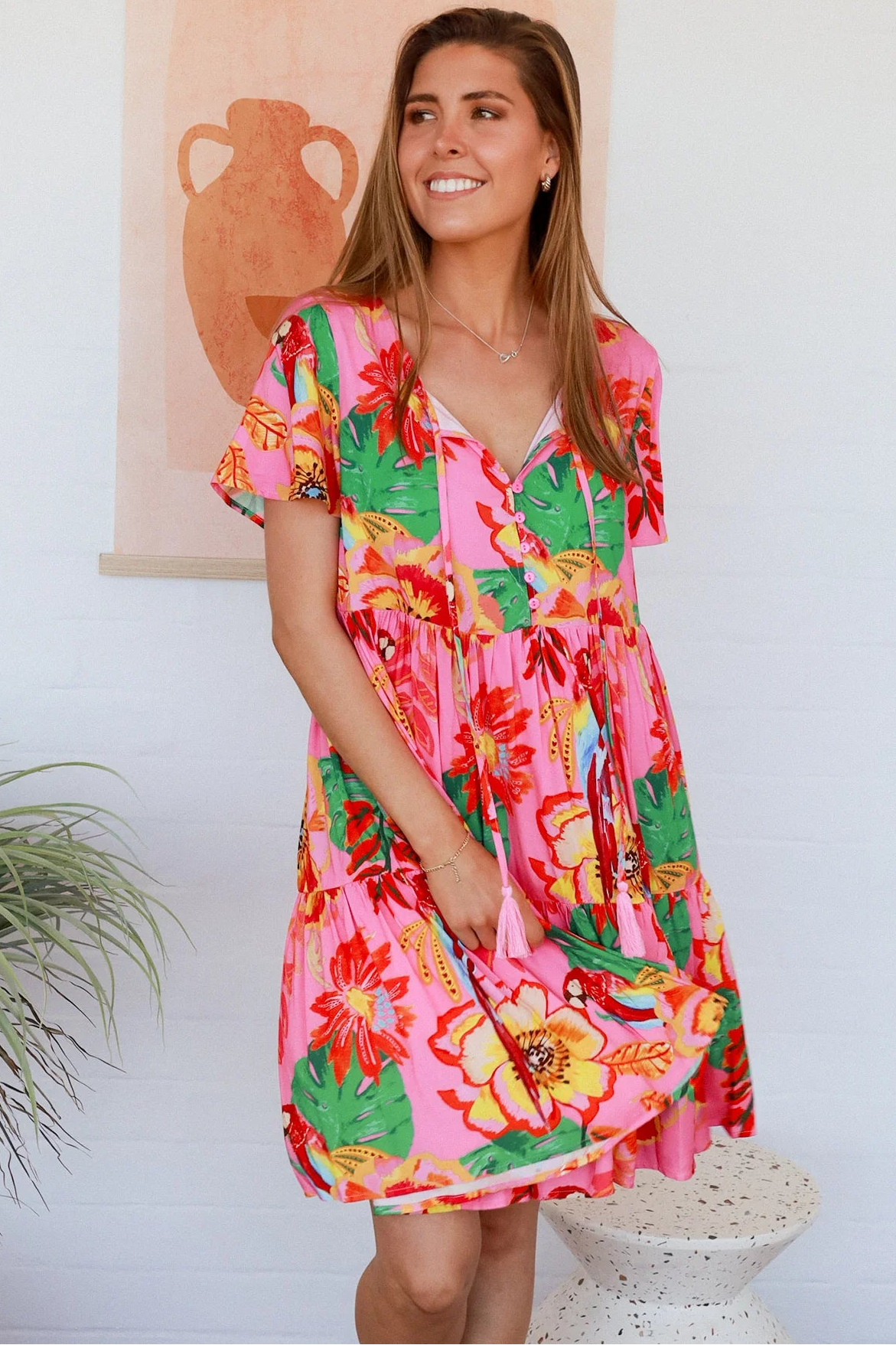 Pink floral mini dress with poppy and parrot print, V-neck button bodice, tassel ties and flutter sleeves