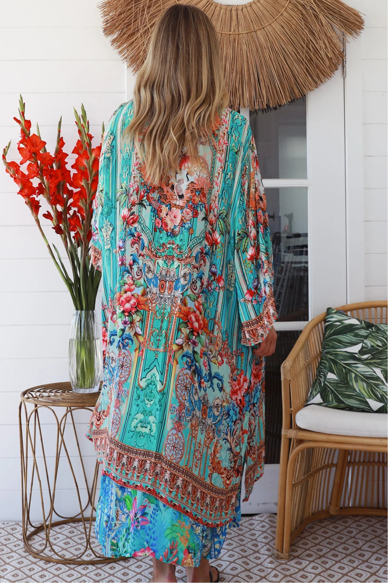 Woman in turquoise floral crepe - viscose kimono with bronze and sapphire border detailing, walking along a sunlit coastal setting - resort luxe boho style.