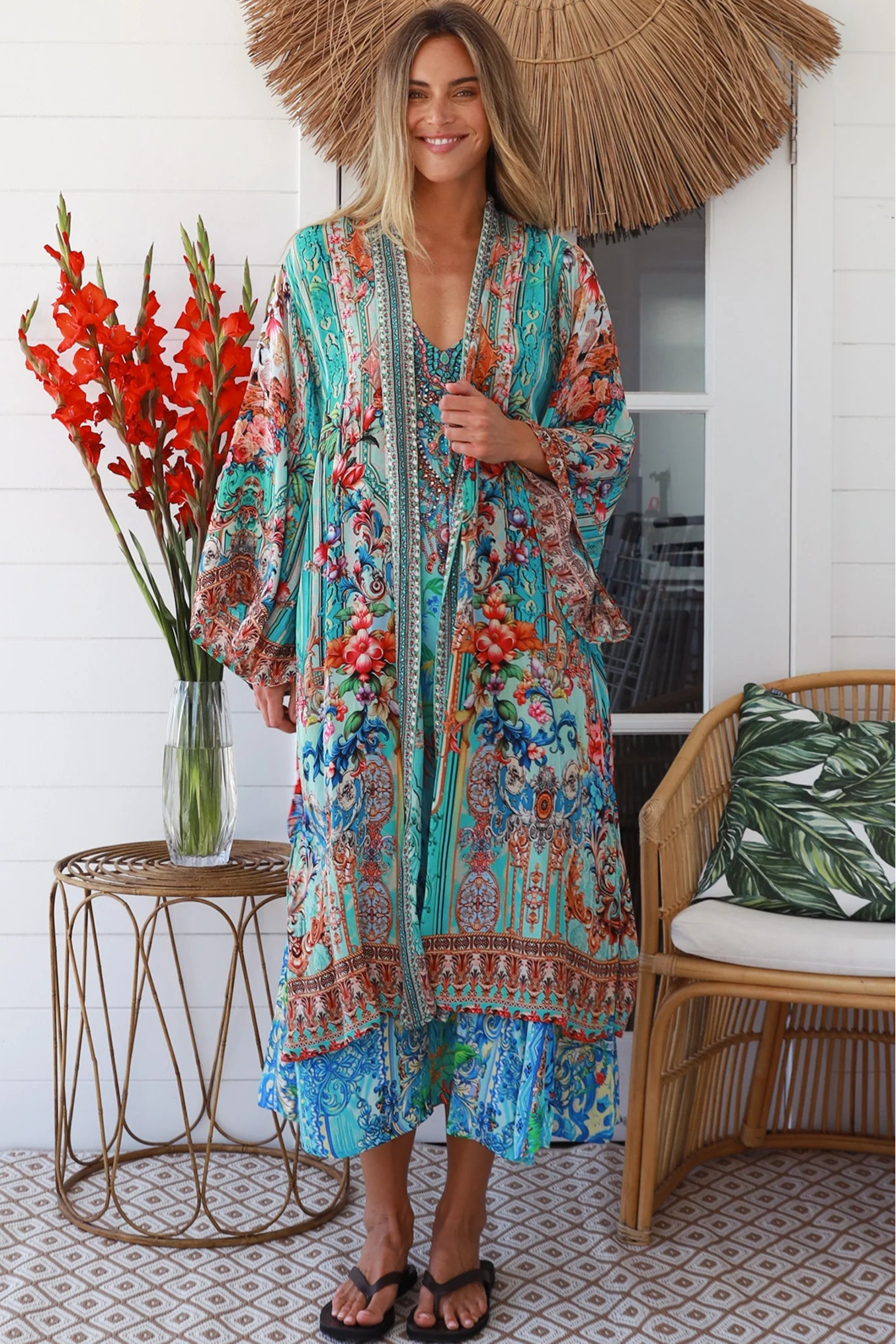 Woman in turquoise floral crepe - viscose kimono with bronze and sapphire border detailing, walking along a sunlit coastal setting - resort luxe boho style.