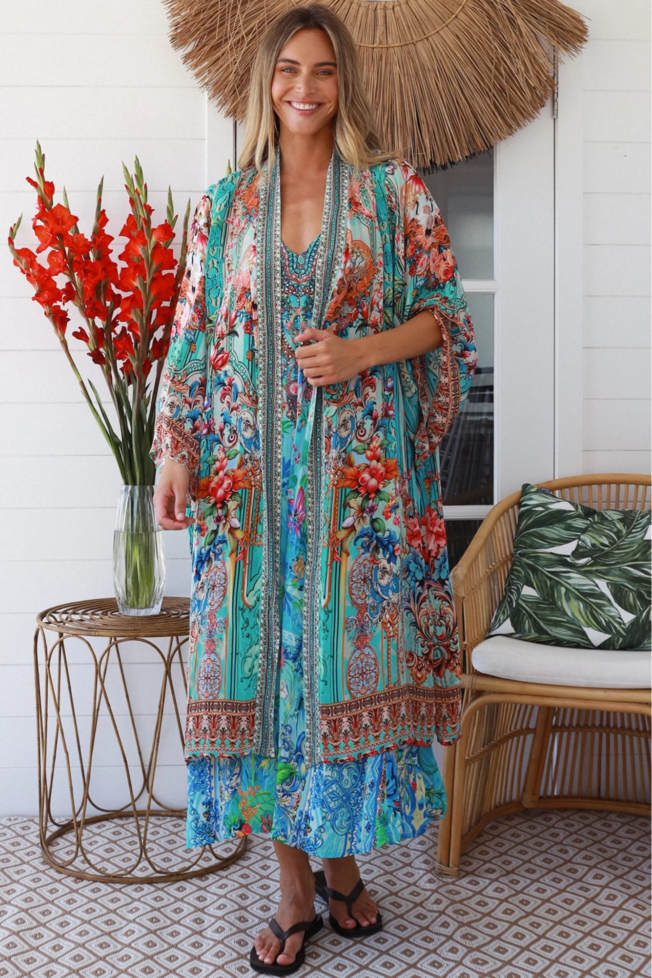 Woman in turquoise floral crepe - viscose kimono with bronze and sapphire border detailing, walking along a sunlit coastal setting - resort luxe boho style.