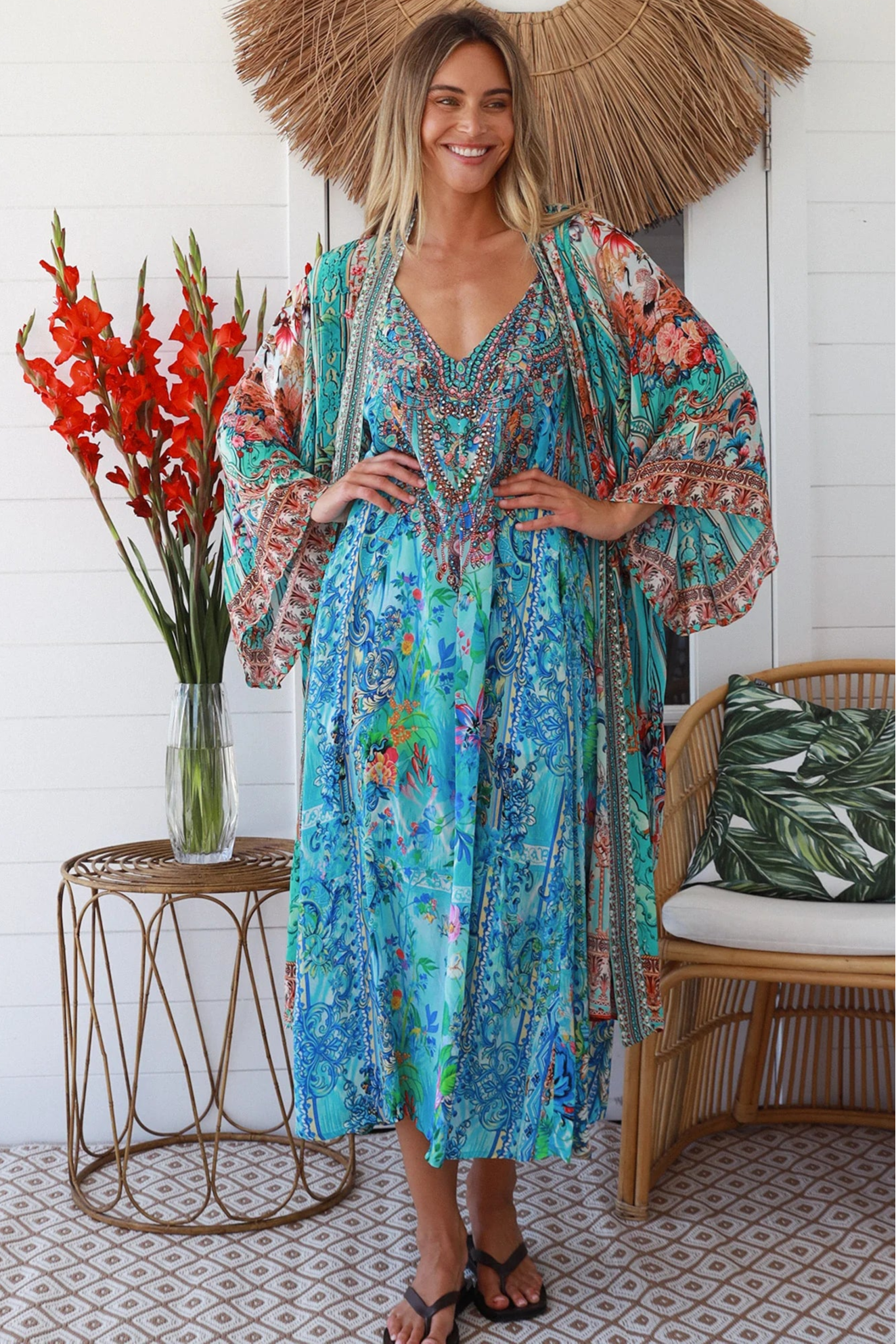 Woman in turquoise floral crepe - viscose kimono with bronze and sapphire border detailing, walking along a sunlit coastal setting - resort luxe boho style.