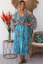 Woman in turquoise floral linen - viscose kimono with bronze and sapphire border detailing, walking along a sunlit coastal setting - resort luxe boho style.