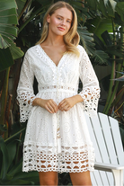 Woman in white cotton embroidered mini dress with daisy crochet waist and fluted bell sleeves – boho summer style