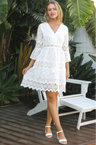 Woman in white embroidered anglaise cotton mini dress with crochet trims and scalloped tiers – Australian boho fashion