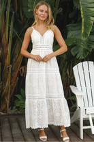 White embroidered cotton maxi dress with lace-trim neckline and scalloped tiered skirt in natural summer light.