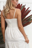 White embroidered cotton maxi dress with lace-trim neckline and scalloped tiered skirt in natural summer light.