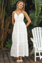 White embroidered cotton maxi dress with lace-trim neckline and scalloped tiered skirt in natural summer light.