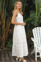 White embroidered cotton maxi dress with lace-trim neckline and scalloped tiered skirt in natural summer light.