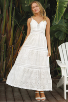 White embroidered cotton maxi dress with lace-trim neckline and scalloped tiered skirt in natural summer light.
