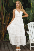 White embroidered cotton maxi dress with lace-trim neckline and scalloped tiered skirt in natural summer light.
