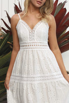 White embroidered cotton maxi dress with lace-trim neckline and scalloped tiered skirt in natural summer light.