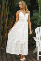 White embroidered cotton maxi dress with lace-trim neckline and scalloped tiered skirt in natural summer light.