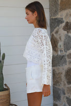 Woman wearing white crochet cotton boho top with long sleeves styled with white shorts Australian fashion
