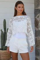 Woman wearing white crochet cotton boho top with long sleeves styled with white shorts Australian fashion