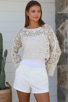 Cream crochet cotton long sleeve crop top with scalloped hem and flared cuffs styled with white shorts