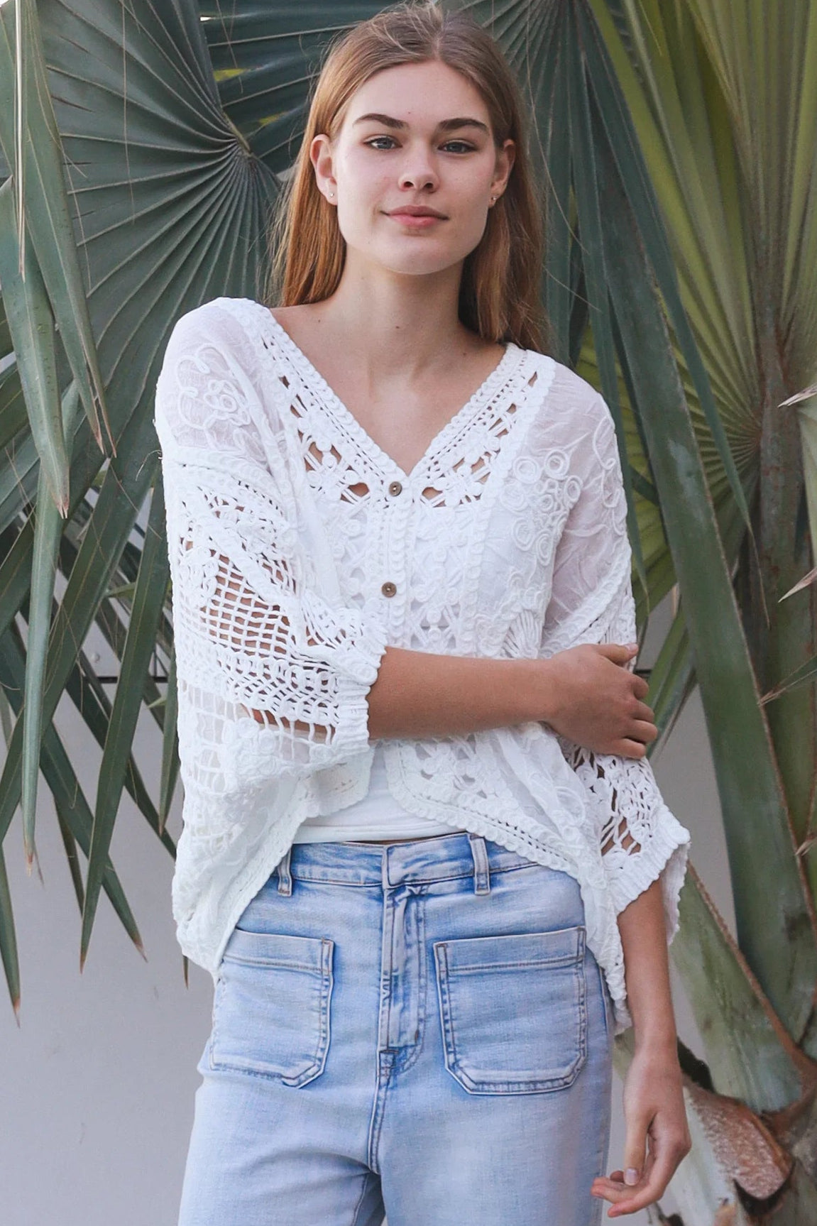 Woman wearing oversized white embroidered cotton crochet blouse with airy sleeves and relaxed coastal bohemian styling in Australia