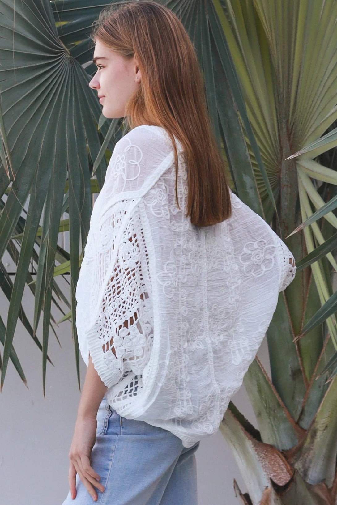 Woman wearing oversized white embroidered cotton crochet blouse with airy sleeves and relaxed coastal bohemian styling in Australia