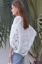 Woman wearing oversized white embroidered cotton crochet blouse with airy sleeves and relaxed coastal bohemian styling in Australia