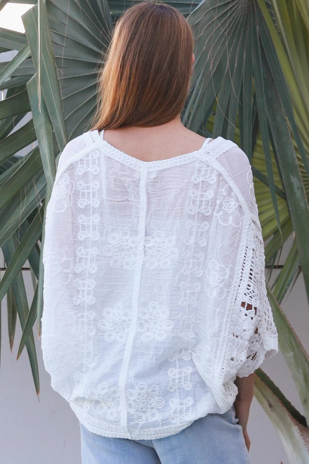 Woman wearing oversized white embroidered cotton crochet blouse with airy sleeves and relaxed coastal bohemian styling in Australia