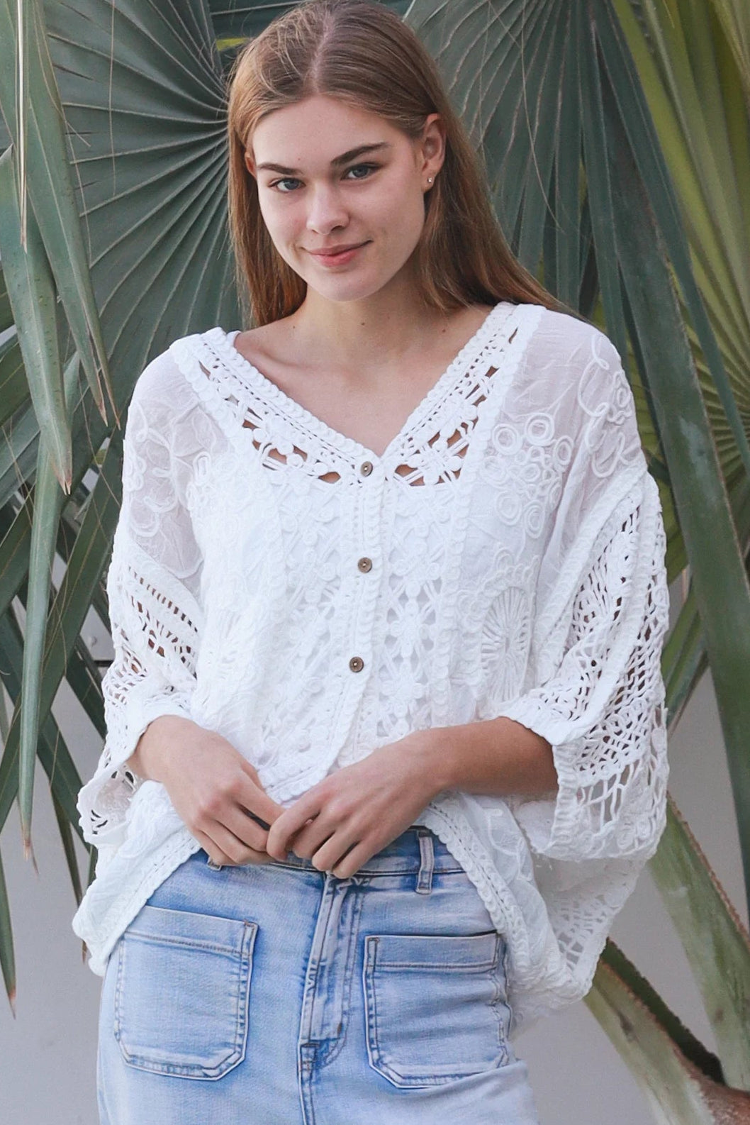 Woman wearing oversized white embroidered cotton crochet blouse with airy sleeves and relaxed coastal bohemian styling in Australia