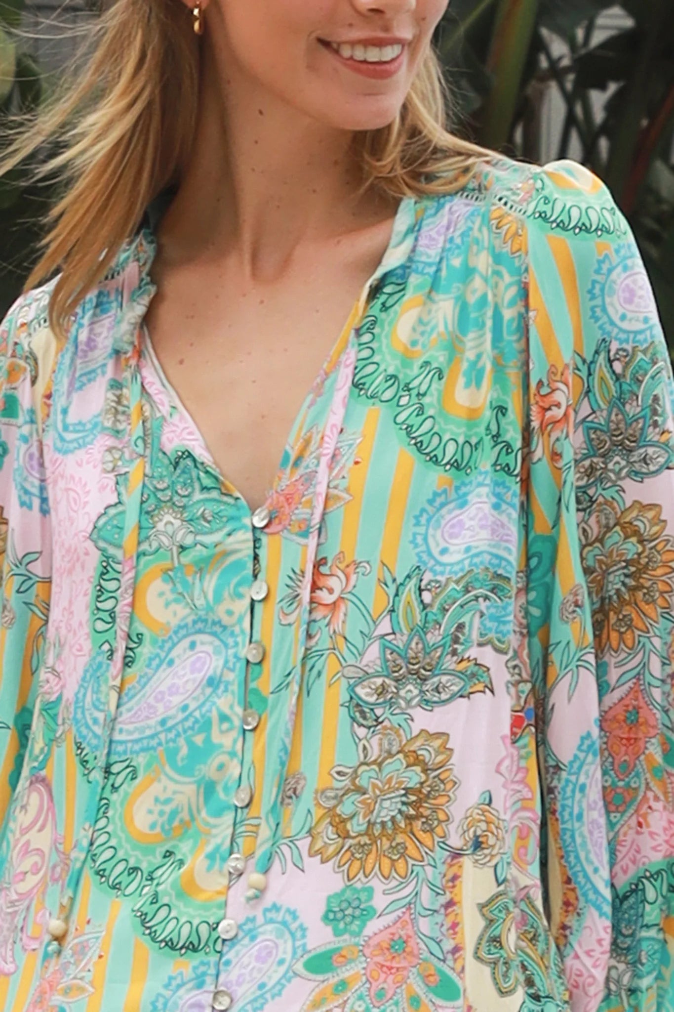 Woman wearing Salty Palm Mika Blouse in green patchwork rayon with V-neck tie, cotton lace shoulders and crochet yoke