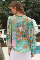 Woman wearing Salty Palm Mika Blouse in green patchwork rayon with V-neck tie, cotton lace shoulders and crochet yoke