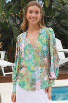 Woman wearing Salty Palm Mika Blouse in green patchwork rayon with V-neck tie, cotton lace shoulders and crochet yoke