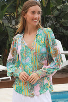 Woman wearing Salty Palm Mika Blouse in green patchwork rayon with V-neck tie, cotton lace shoulders and crochet yoke