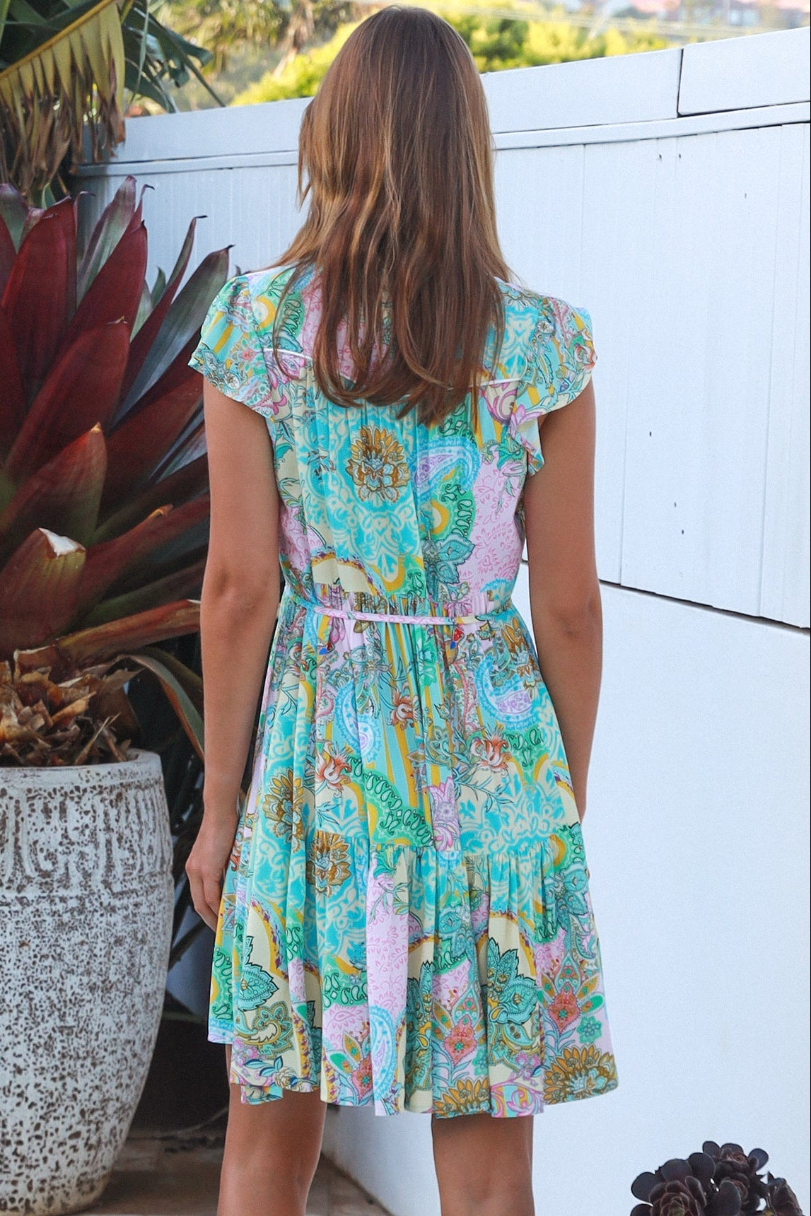 Woman wearing a green and pink painterly patchwork rayon mini dress with flutter sleeves and waist tie by Salty Palm