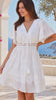 Model in motion wearing the Angelique white embroidered cotton mini dress by Salty Palm with lace V-neck, tassel ties, flutter sleeves and tiered skirt. | Bohemian Love Runway 