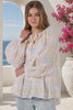 A woman wearing a light pink eyelet blouse with a multicolor pastel geometric pattern, featuring a tie-neck detail and long sleeves, paired with light-wash jeans in an outdoor setting with a sea view background in motion from Bohemian Love Runway
