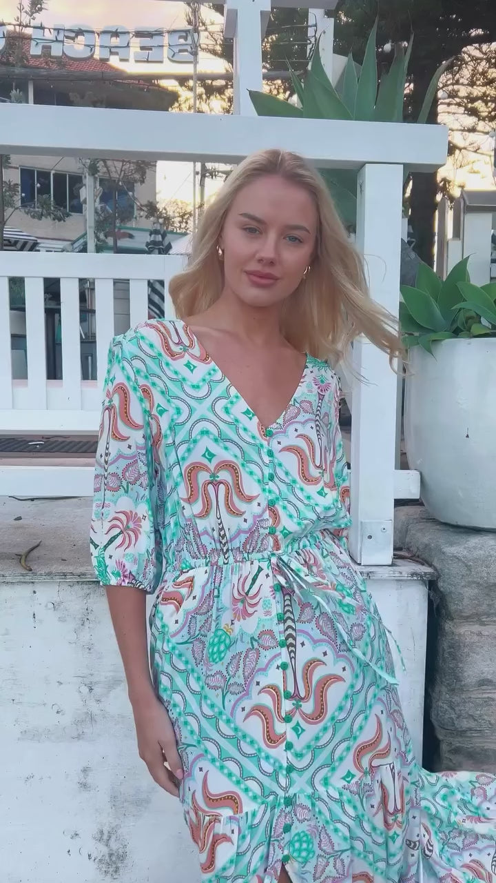 Model wearing Fiorella green rayon boho maxi dress with V-neck and tie waist, walking outdoors - bohemian fashion.
