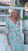 Model wearing Fiorella green rayon boho maxi dress with V-neck and tie waist, walking outdoors - bohemian fashion.