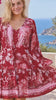 Model in motion wearing the Claudette ruby red floral boho mini dress with blouson sleeves, drawstring waist, pockets and border print frill hem at Bohemian Love Runway 