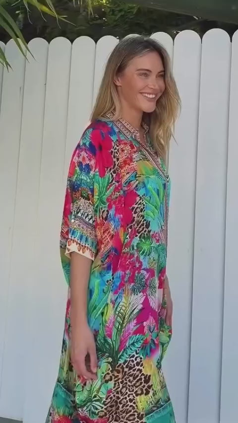 Woman wearing a tropical print viscose linen midi dress with bright coral, aqua, and green hues walking through sunlight - Resort Luxe bohemian style Australia