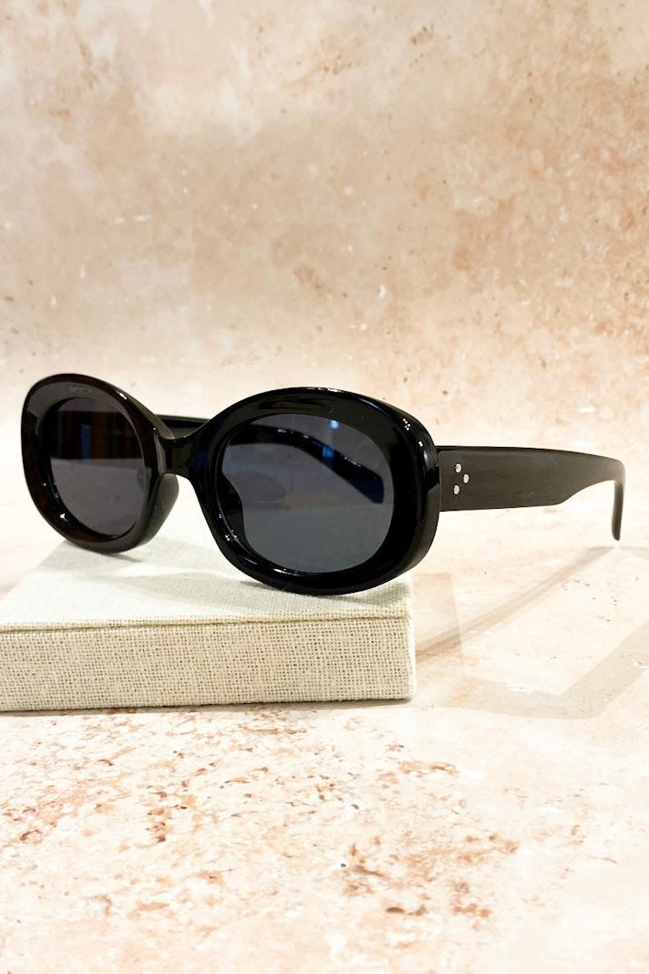 Black oversized oval sunglasses with tinted lenses styled on neutral block - vintage flat lay fashion Australia.